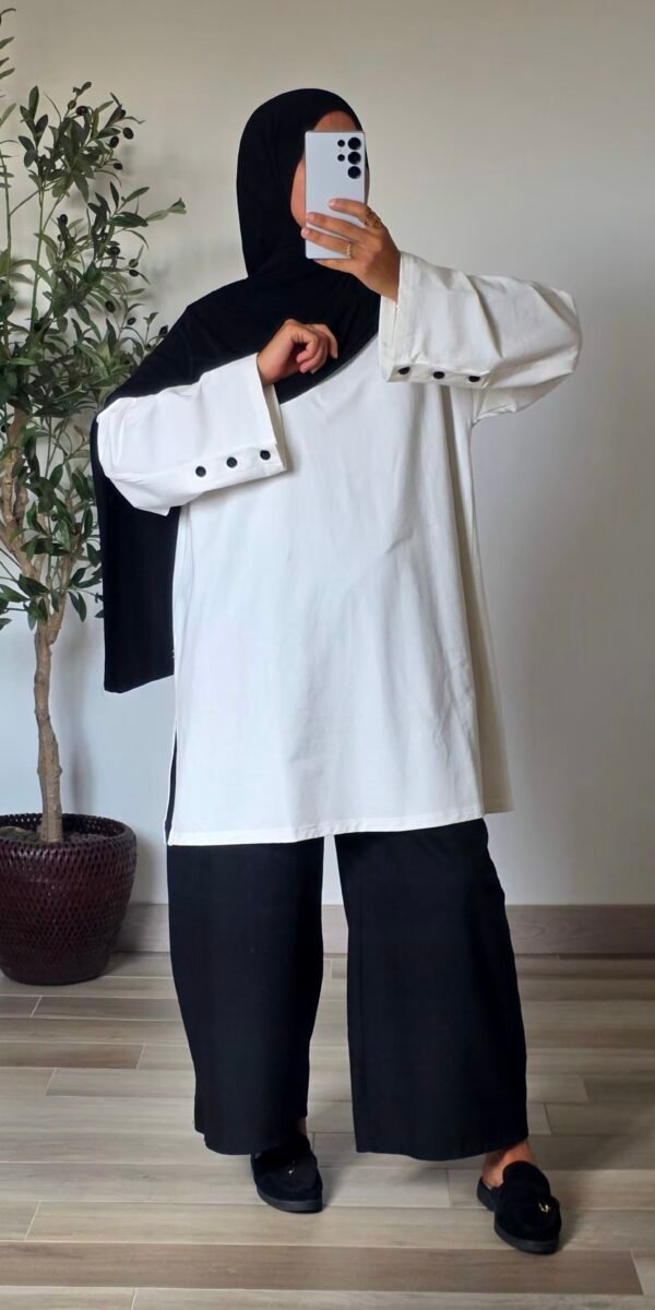 Femme portant un t-shirt long oversize blanc à manches longues avec boutons noirs aux poignets