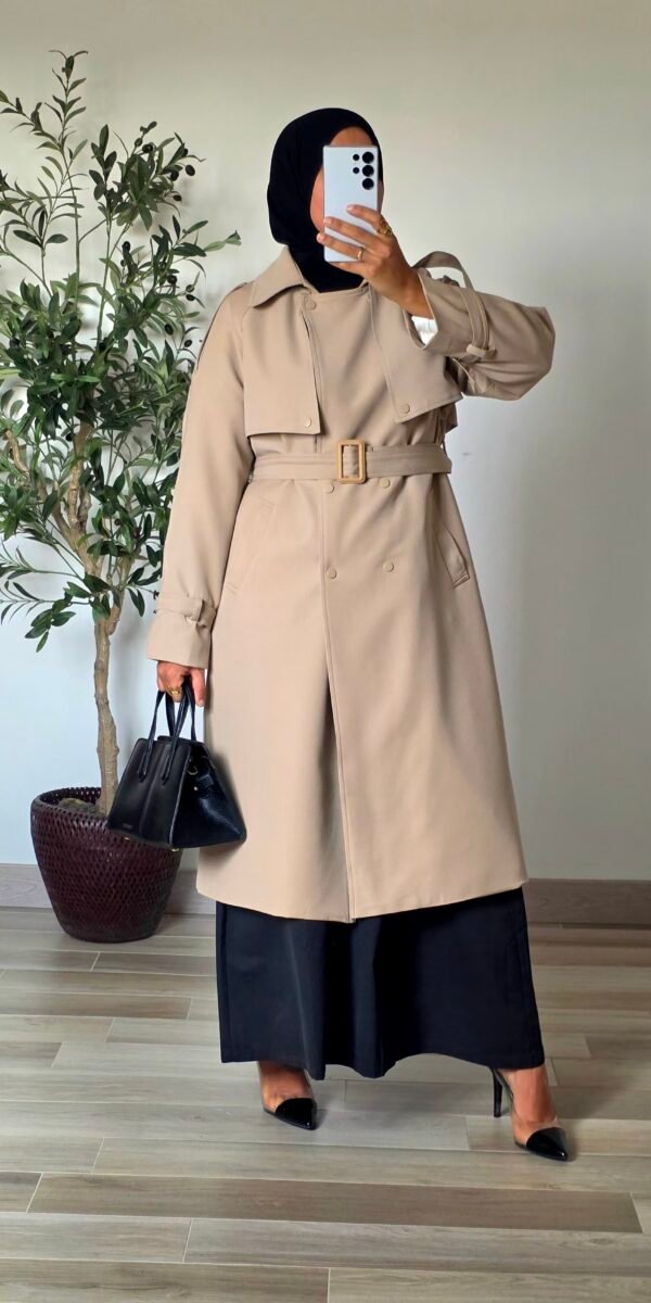 Femme portant un trench long beige classique avec ceinture et jupe longue noire