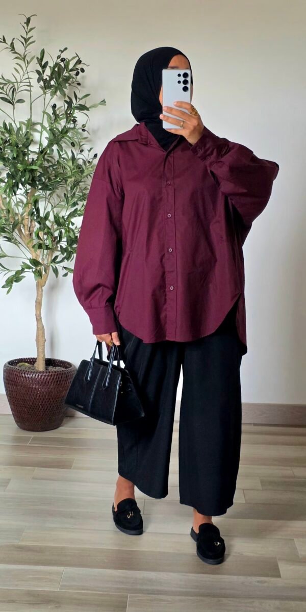 Femme portant une chemise longue oversize bordeaux en coton avec une jupe longue noire