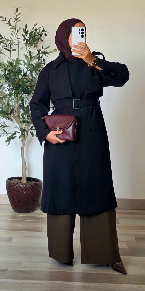Femme portant un trench long noir classique avec ceinture et jupe longue noire
